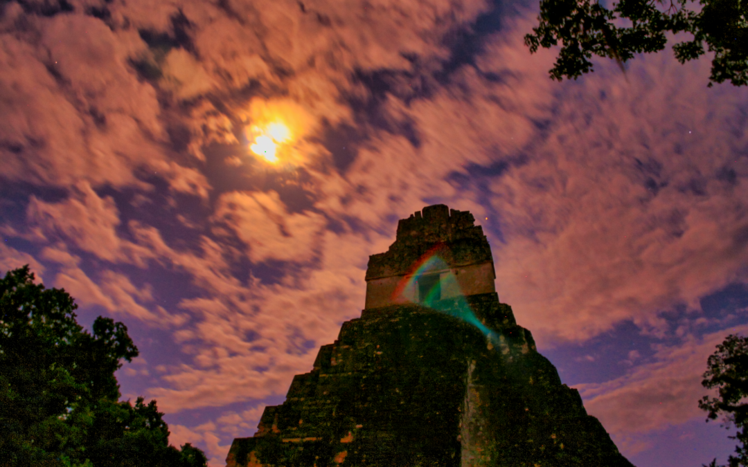 "Moon emerging behind clouds over the Great Jaguar Temple in Tikal National Park, illustrating the Tikal National Park Frequently Asked Questions topic."